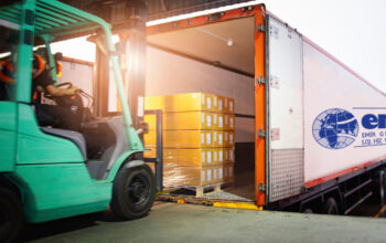 Forklift Tractor Loading Package Boxes on Pallet into Cargo Container. TrailerTruck Parked Loading at Dock Warehouse. Shipment Delivery. Supply Chain. Shipping Logistics Freight Truck Transportation.